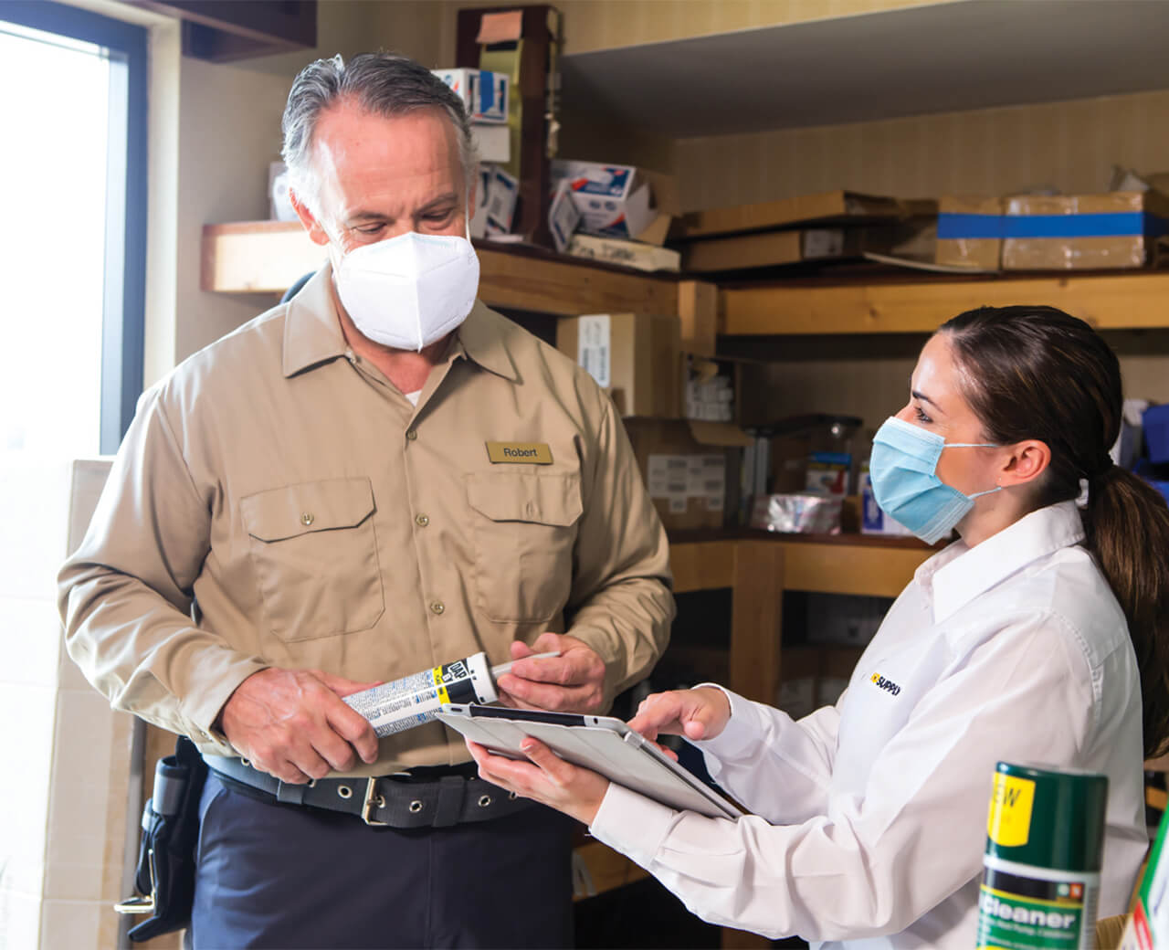 2 HD Supply personnel wearing masks and looking at a tablet in a warehouse.