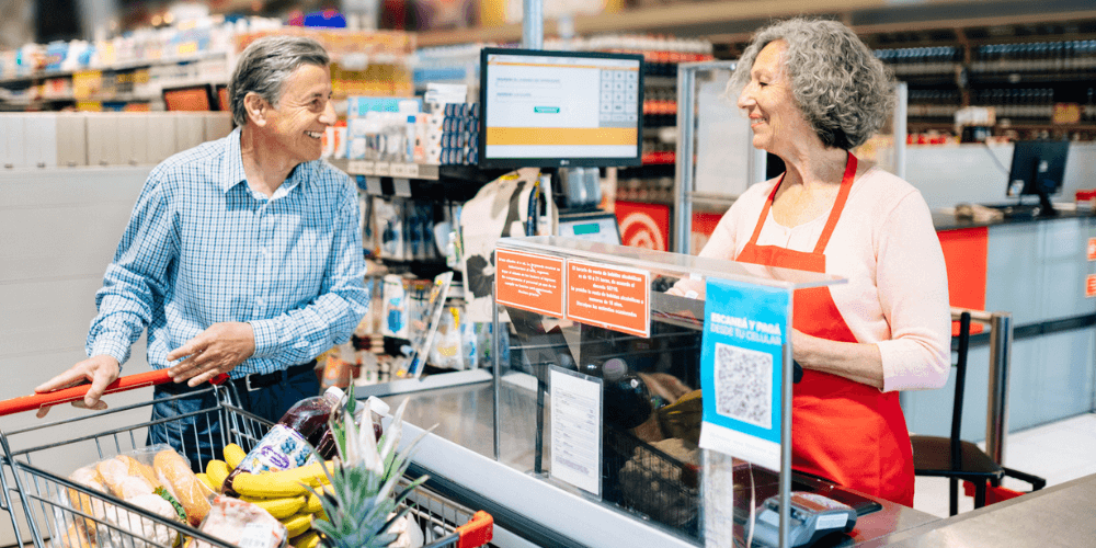 Woman cashier talks to man pushing cart full of groceries