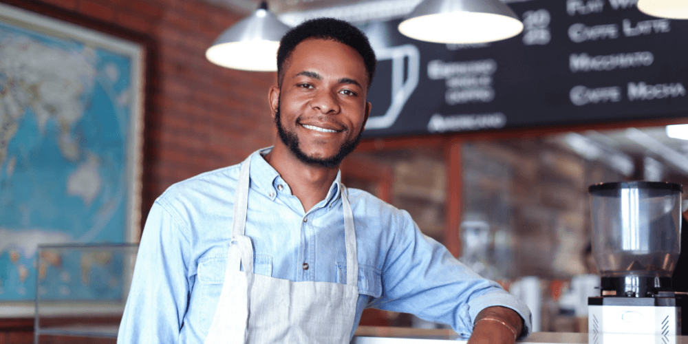 Man in an apron leans against the counter in a coffee shop
