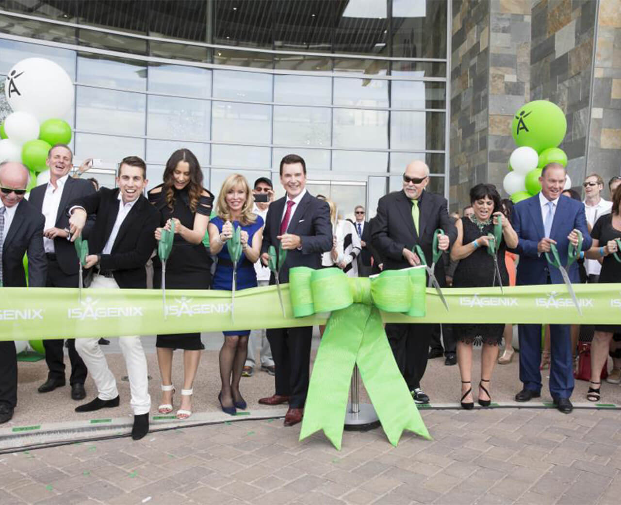 Isagenix employees cutting a large green ribbon outside a new building